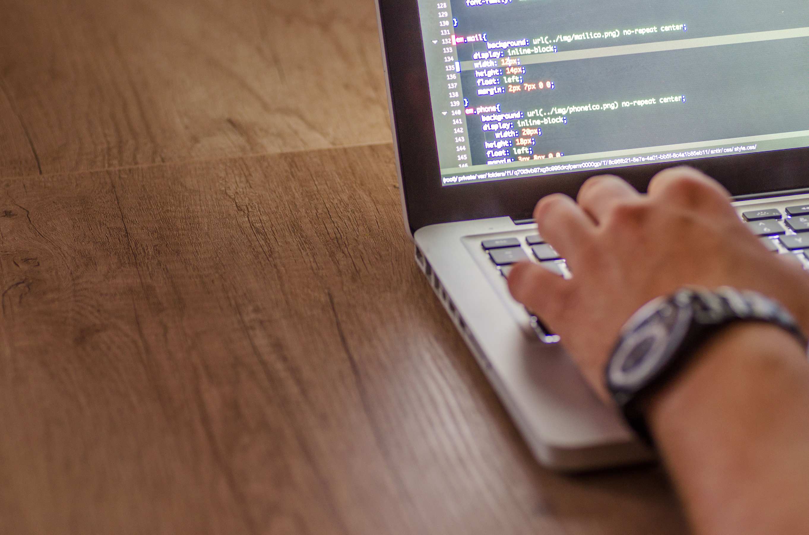 Wide view of a developer workspace with laptop on a desk — person coding on a laptop, web development and programming