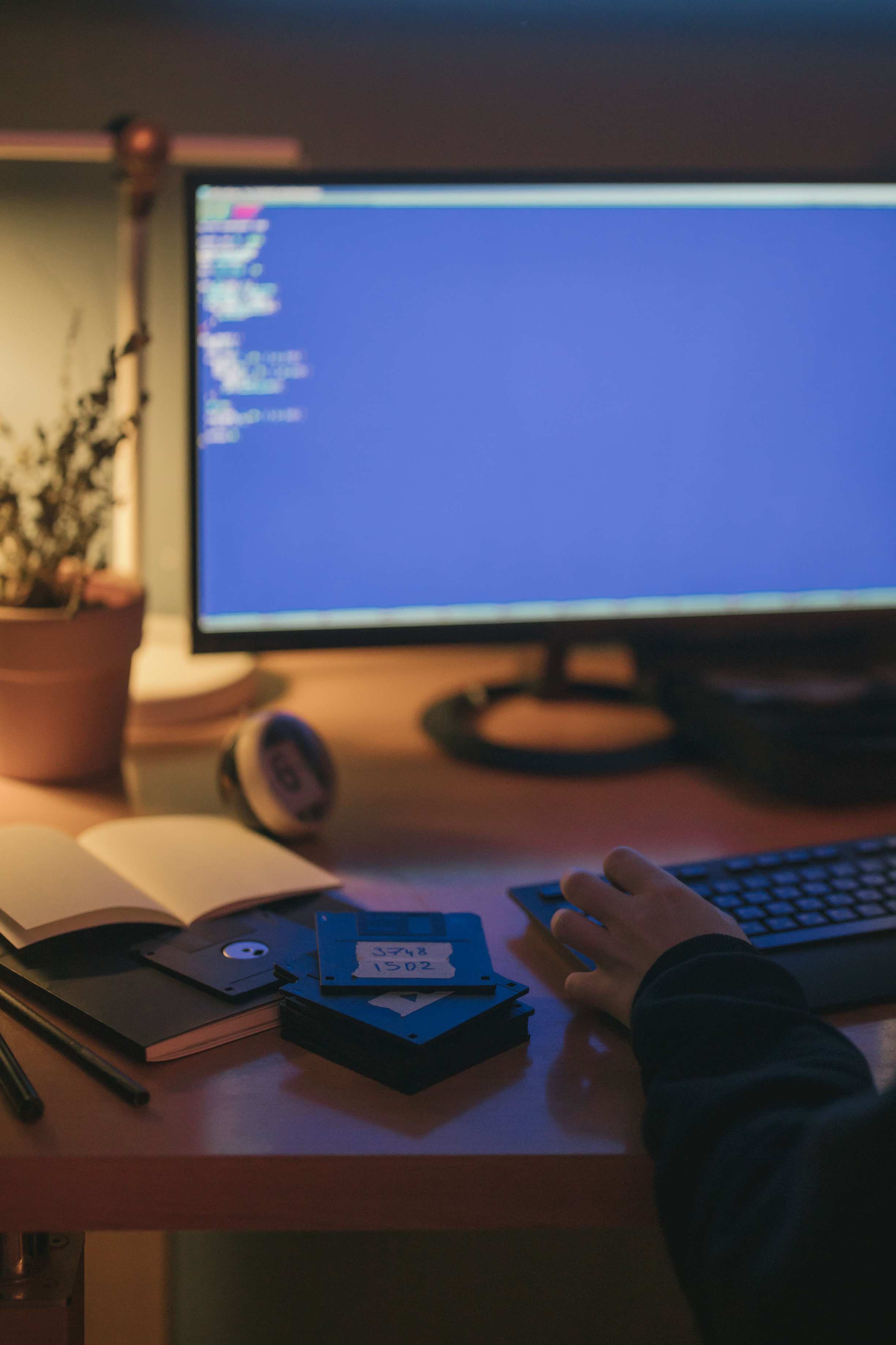 Overhead view of hands at a keyboard with code on screen — home office with a computer screen displaying code